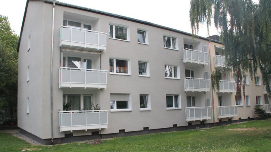 Mehrfamilienhaus mit grauem Fassadenanstrich und weißen Balkonen